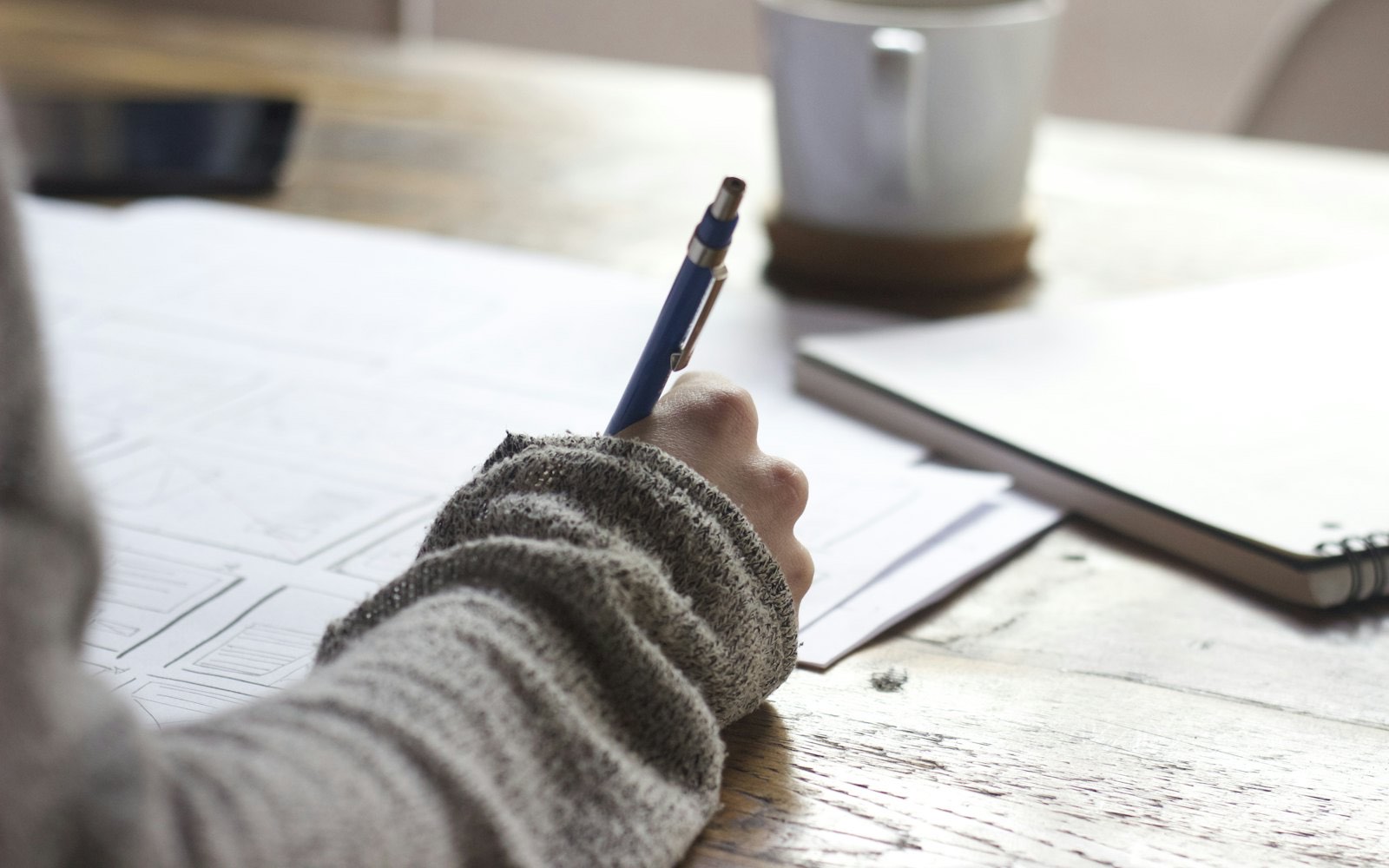 A student writing at a desk beside a bright window